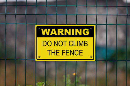 Black and Yellow warning sign attached on a fence. The sign stating âWarning - Do not climb the fenceâ.の写真素材