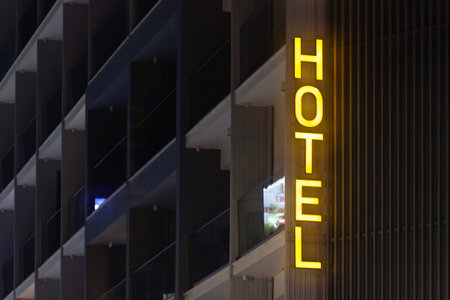Vertical yellow hotel sign at the egde of a building illuminated by night.の写真素材