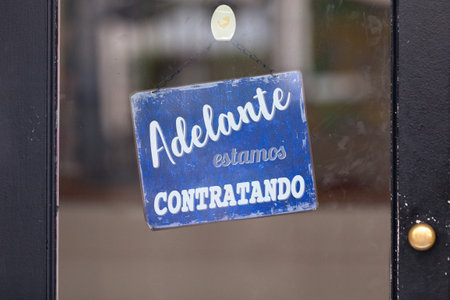 Red open sign with written in it in Spanish: "Adelante, estamos contratando", meaning in English "Come in, we're hiring".の写真素材