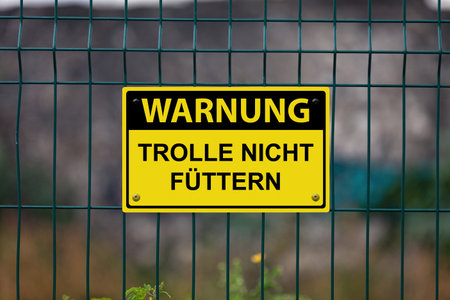 Yellow warning sign on a fence stating in German: "Warnung - Trolle nicht fÃ¼ttern", meaning in English "Warning - Don't feed the trolls".の写真素材