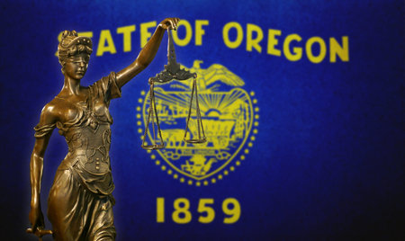Close-up of a small bronze statuette of Lady Justice before a flag of Oregon.の写真素材