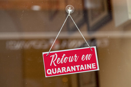 Red sign hanging at the glass door of a shop with written in French Retour en quarantaine, meaning...