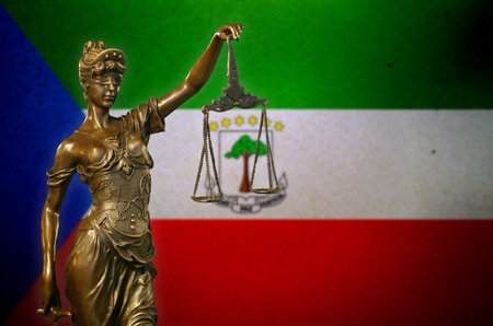 Close-up of a small bronze statuette of Lady Justice before a flag of Equatorial Guinea.の写真素材