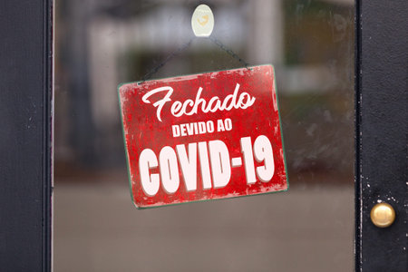 Red closed sign with written in it in Portuguese Fechado devido ao COVID-19 meaning in English...