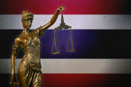 Close-up of a small bronze statuette of Lady Justice before a Thai flag.の写真素材