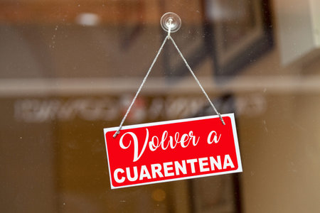 Red sign hanging at the glass door of a shop with written in Spanish "Volver a cuarentena" meaning in English "Back to quarantine".の写真素材