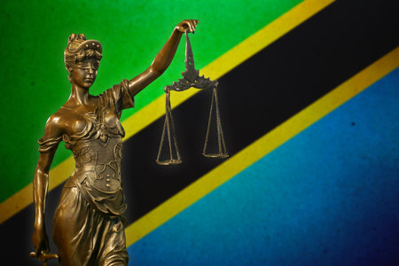 Close-up of a small bronze statuette of Lady Justice before a flag of Tanzania.の写真素材
