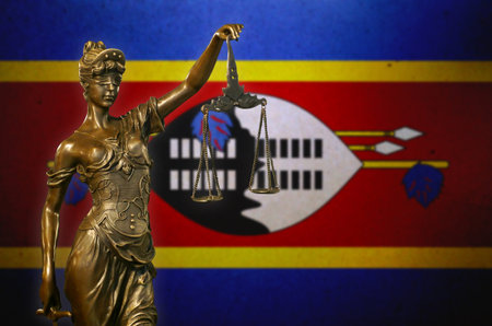 Close-up of a small bronze statuette of Lady Justice before a flag of Swaziland.の写真素材