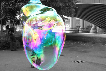 Young woman making a huge bubble on the bank of the Thames near a bridge. To focus on the bubble,...