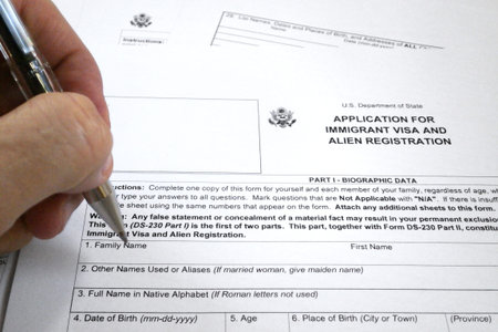 A pen hold by the fingers of somebody ready to fill an application form for immigrant visa and alien...