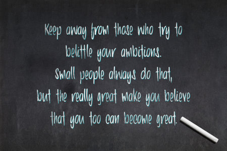 Blackboard with a quote from Mark Twain saying "Keep away from those who try to belittle your ambitions. Small people always do that, but the really great make you believe that you too can become great.", drawn in the middle.の写真素材