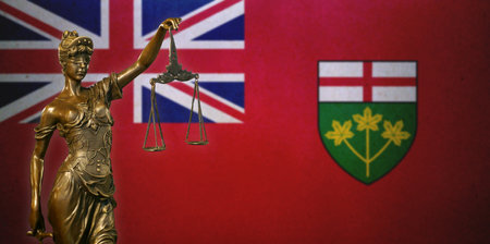 Close-up of a small bronze statuette of Lady Justice before a flag of Ontario (Canada).の写真素材