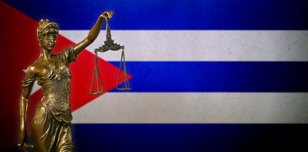 Close-up of a small bronze statuette of Lady Justice before a Cuban flag.の写真素材
