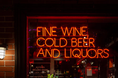 A red neon light shaped into the phrase Fine wine, cold beer and liquors on the window of a bar.