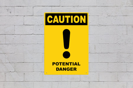 Yellow warning sign screwed to a cinder block wall to warn about a threat. In the middle of the...
