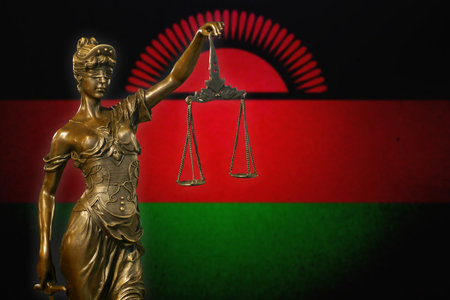 Close-up of a small bronze statuette of Lady Justice before a flag of Malawi.の写真素材