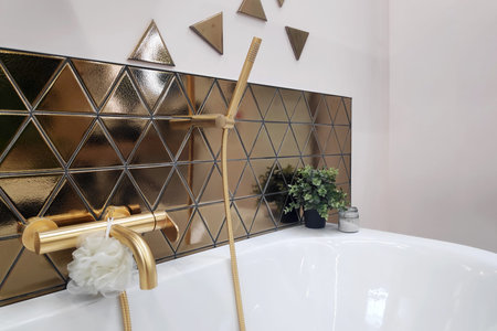 Luxurious and modern design bathroom, featuring gold triangular tiles, matte gold fixtures, and minimalist decor with a touch of greenery.の写真素材