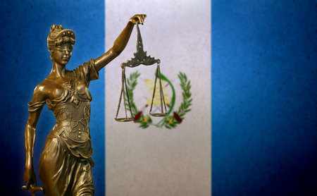 Close-up of a small bronze statuette of Lady Justice before a flag of Guatemala.の写真素材