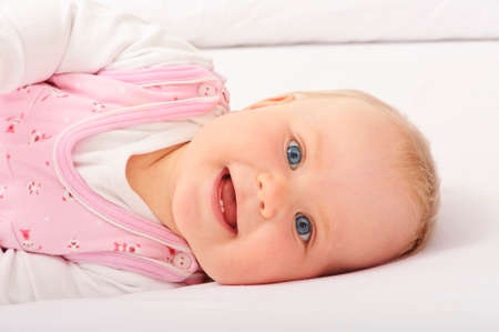 Baby lying down on bed and smiling at cameraの写真素材
