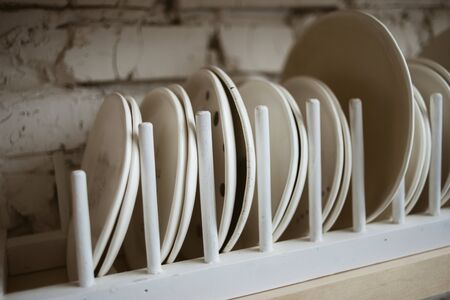 Ceramic white plates in rustic wooden dish holder on shelf with white brick wall in backgroundの写真素材