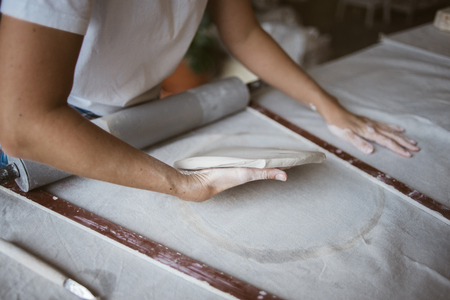 Sculptor carefully puts grey raw clay on big table with industrial fabric in workshopの写真素材
