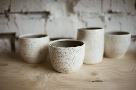 Glazed white ceramic rustic cups on wooden shelf in pottery workshopの写真素材