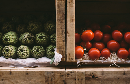 Healthy natural artichokes and fresh tomatoes in wooden boxes on vegetables market, close viewの写真素材