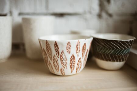 Glazed ceramic painted cups with pattern on wooden shelf in studioの写真素材