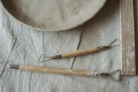 Pottery tools with wooden holders and raw clay plate on table with industrial fabric in pottery studioの写真素材