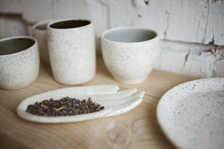 Stylish chamotte ceramic glazed hand with dry lavender and handmade cups on wooden shelf with white brick wall on background in workshopの写真素材