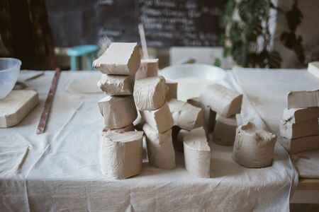 Pieces of grey raw clay for modeling ceramic ware on big table with industrial fabric in workshopの写真素材