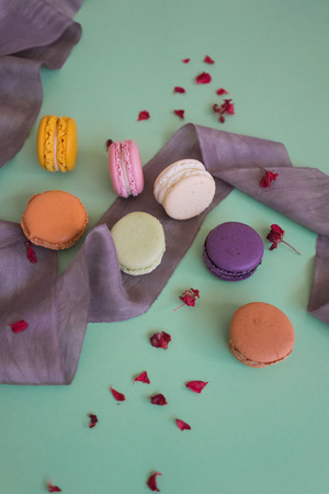 Colored fresh macaroons with silk lilac ribbon and little petals on light green backgroundの写真素材