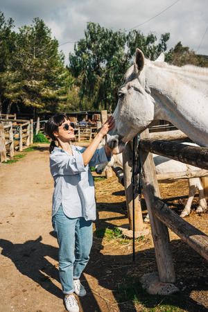 Brunette young lady stroking big white horse on ranchの写真素材