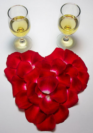 Photo of a heart shape made of rose petals with two glasses of champagne above itの写真素材