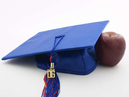 Graduation hat and tassel next to a red apple isolated on whiteの写真素材