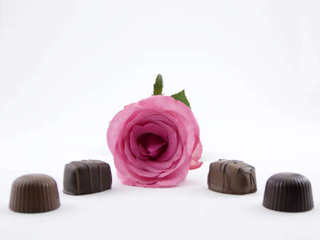 Photo of a pink rose and several pieces of chocolate by itの写真素材