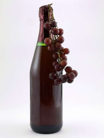 Photo of a wine bottle with red grapes hanging from itの写真素材