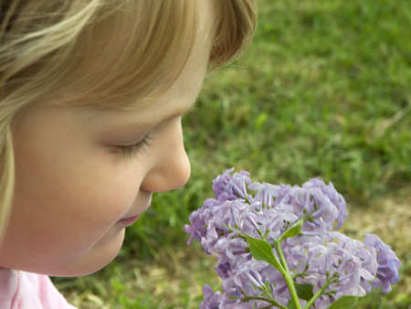 Photo of a girl smelling flowers out in the grassの写真素材