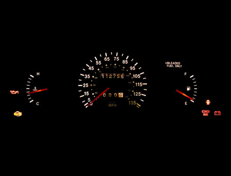 Car dashboard gauges illuminated on black background