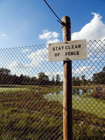 Swamp land fenced in with a sign that reads, stay clear of fenceの写真素材