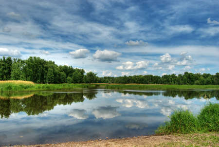 HDR photo of trees and sky reflecting off lakeの写真素材