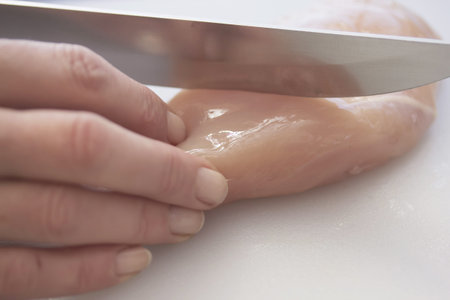 Women Hand sliced ââfresh chicken breast with a knife on the white deskの写真素材