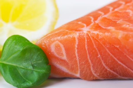 Big salmon, lemon and a basil leaf on white plateの写真素材