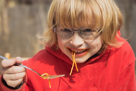 Smiling blond boy with glasses eats spaghetti  Horizontally の写真素材