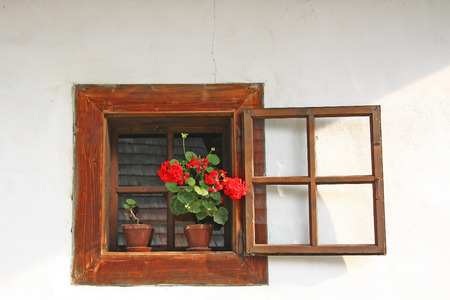 Old wooden window in a rural house with white wall. Red flower in a potの写真素材