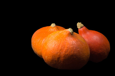 Three orange hokkaido pumpkins on a black background.の写真素材
