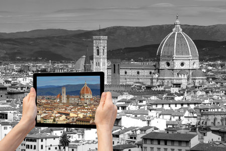 In the bottom left of the photo are hands holding tablet, whose screen contains color photo of the Cathedral Santa Maria del Fiore in Florencel. Background of the photo contains monochromatic photo of the historic center of Florence (Tuscany, Italy)の写真素材