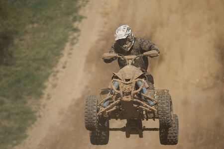 Front view of guad racer jumping. The quad bike and rider are very muddy.Potential trademarks are removed and face of the racer is unidentifiable.の写真素材