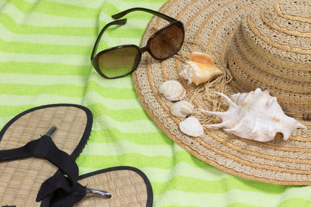 Straw hat, sunglasses, beach sandals and seashells are lying on the green towel.