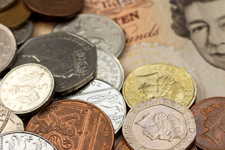 Closeup view of British coins lying on Ten pound banknote with a part of the portrait of the British...